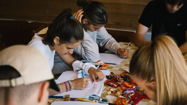 Účastníci pracujú na zadaní pri stole plnom fixiek a sladkostí