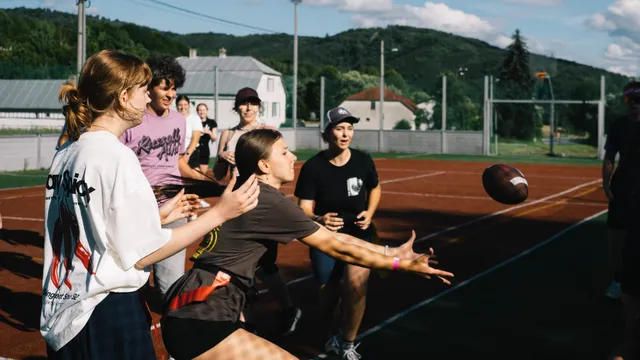 Účastníčky si na ihrisku prihrávajú loptu na americký futbal
